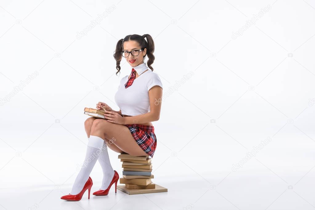 attractive young schoolgirl sitting on stack of books isolated on white