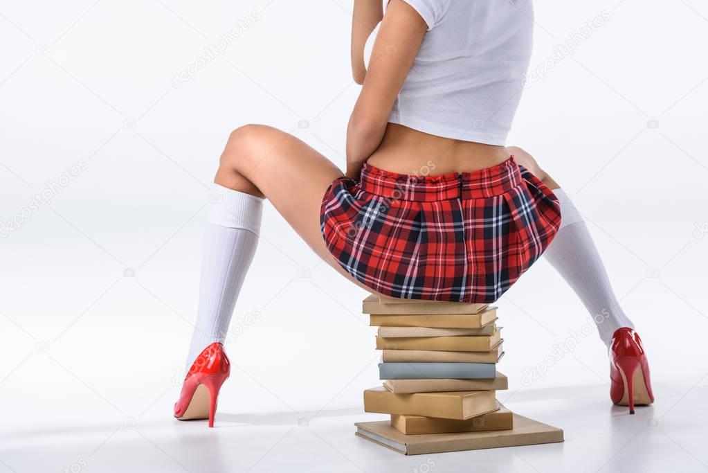 cropped shot of sexy schoolgirl sitting on stack of books on white