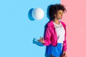 attraktives Mädchen steht gegen Wand und wirft Ball auf rosa und blauem Hintergrund
