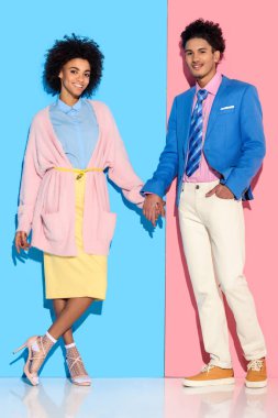 Young african amercian smiling girl and guy holding hands on pink and blue background  clipart