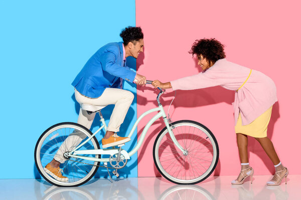 Happy couple having fun with bicycle on pink and blue background