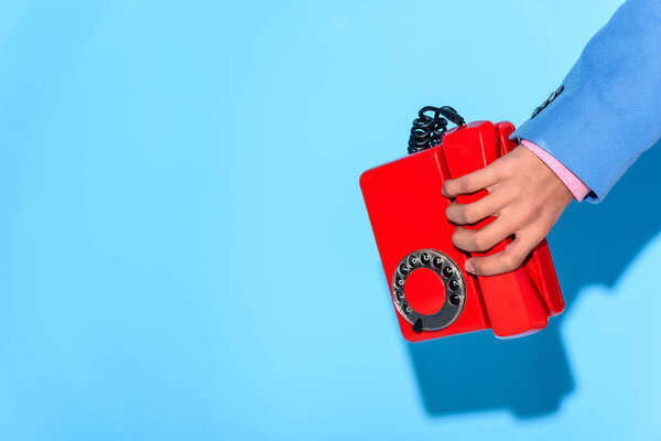 Обрезанное изображение человека в куртке с ретро-телефоном в руке, на синем фоне
