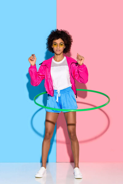 Sporty woman posing while exersizing with hoop and looking at camera on pink and blue background  