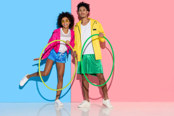 Sporty couple standing with hoops and looking to camera on pink and blue background  