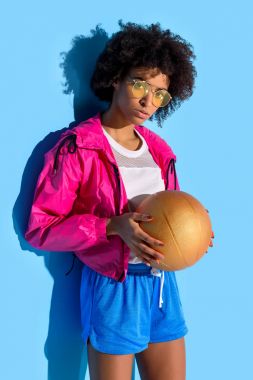  Basketbol topu tutarak ve kameraya mavi arka plan üzerinde seyir gözlüklü genç kız    