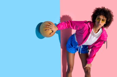  Basketbol topu tutarak ve uzak pembe ve mavi arka plan üzerinde seyir gözlüklü genç kız  