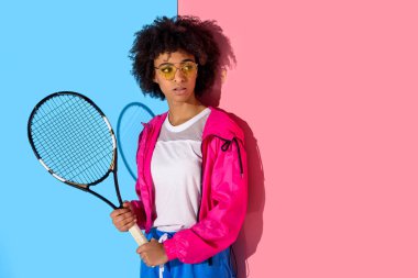 Genç parlak Afro-Amerikan kız pembe ve mavi arka plan üzerinde tenis raketi ile 