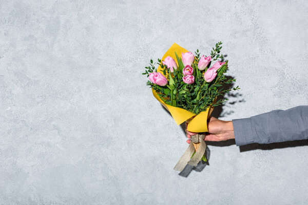 Close-up view of man giving bouquet of flowerson grey background 