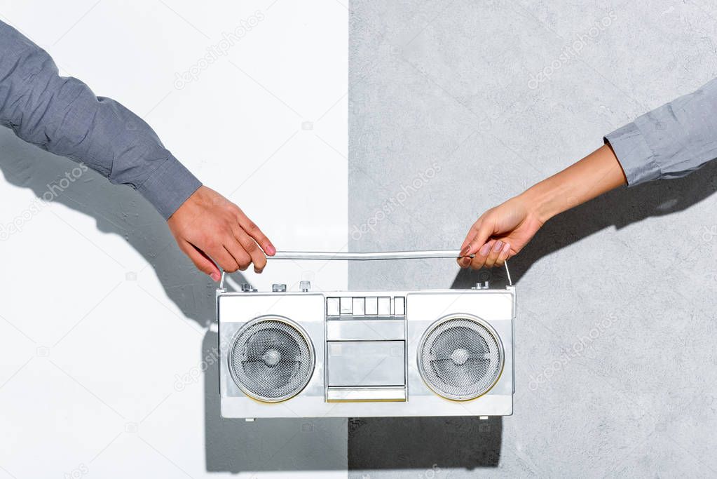 Close-up view of young couple holding boombox in hands on grey and white background 