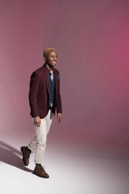 Kırmızı ceketli, pembe arka plan yürüyüş Afrikalı adamı gülümseyen    