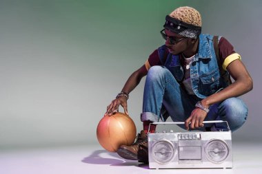 young african american man crouching with golden basketball ball and silver tape recorder on grey clipart