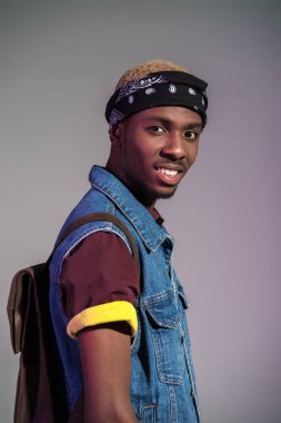 Deri sırt çantası gri izole kamera gülümseyen yakışıklı genç Afro-Amerikan adam portresi