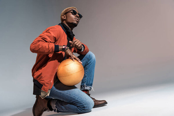 Stylish young african american man holding basketball ball on his knee