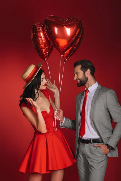 boyfriend presenting balloons to girlfriend isolated on red