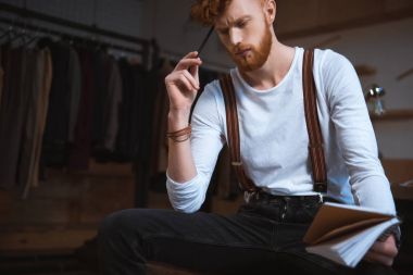 düşünceli genç erkek moda tasarımcısı ile defter ve kalem işyerinde oturan