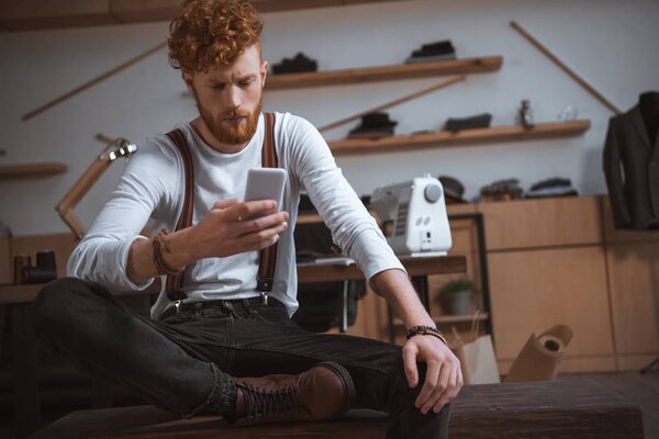 стильный молодой дизайнер, использующий смартфон на рабочем месте
