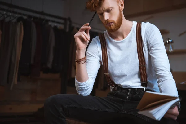 Thoughtful Young Male Fashion Designer Notebook Pencil Sitting Workplace — Free Stock Photo