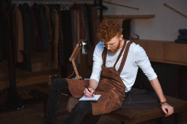genç erkek moda tasarımcısı önlük ve çekici Notlar not defterinde gözlük