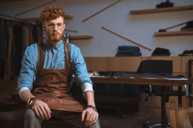 önlük ve Atölyesi'nde oturan gözlük ciddi erkek moda tasarımcısı