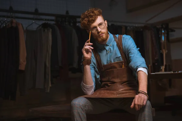 Pensive Young Fashion Designer Apron Holding Pencil Looking Away Workplace — Stock Photo, Image