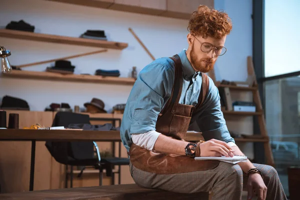 Joven Diseñador Moda Masculino Delantal Gafas Tomando Notas Taller — Foto de stock gratis