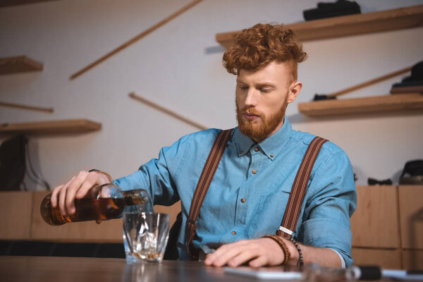 handsome stylish young man pouring whisky from bottle in glass