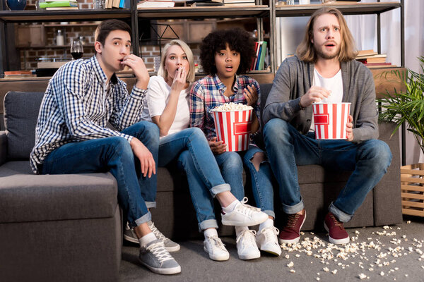 Shocked multiethnic friends watching horror movie with popcorn