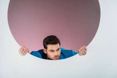stylish bearded young man looking through hole on grey  clipart