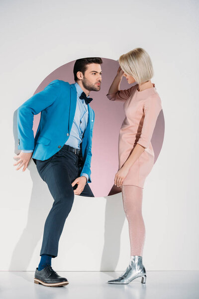fashionable couple in love looking at each other while stepping through hole on grey  