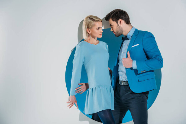 beautiful fashionable young couple looking at each other while standing in blue aperture on grey