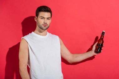 handsome young man holding beer bottle and looking at camera on pink clipart