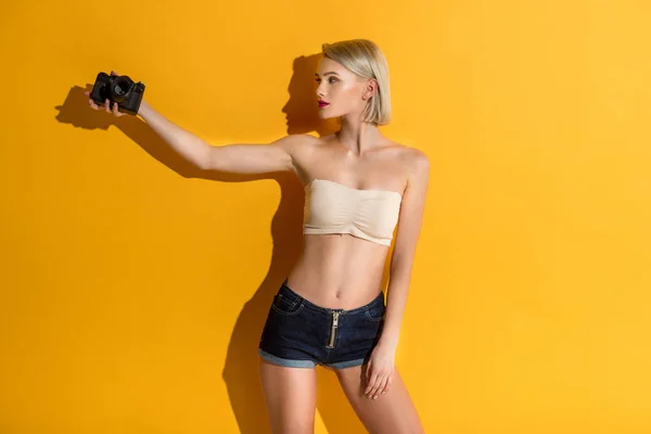 Beautiful Young Blonde Woman Holding Camera Looking Away Yellow — Stock Photo, Image