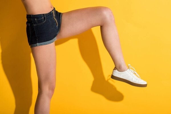 cropped shot of girl in denim shorts posing on yellow