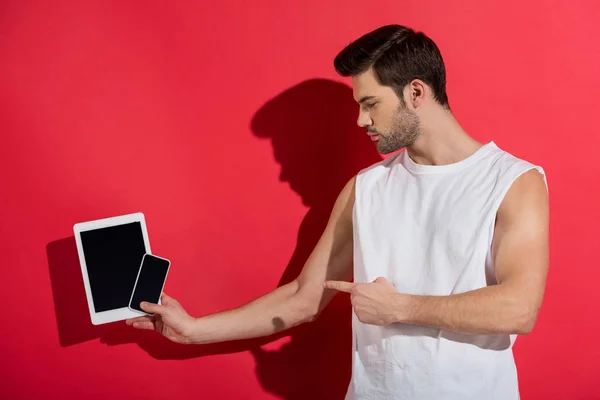 Jovem Bonito Segurando Smartphone Com Tablet Digital Apontando Com Dedo — Fotos gratuitas