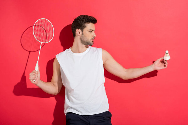 handsome young man holding badminton racket and shuttlecock on pink