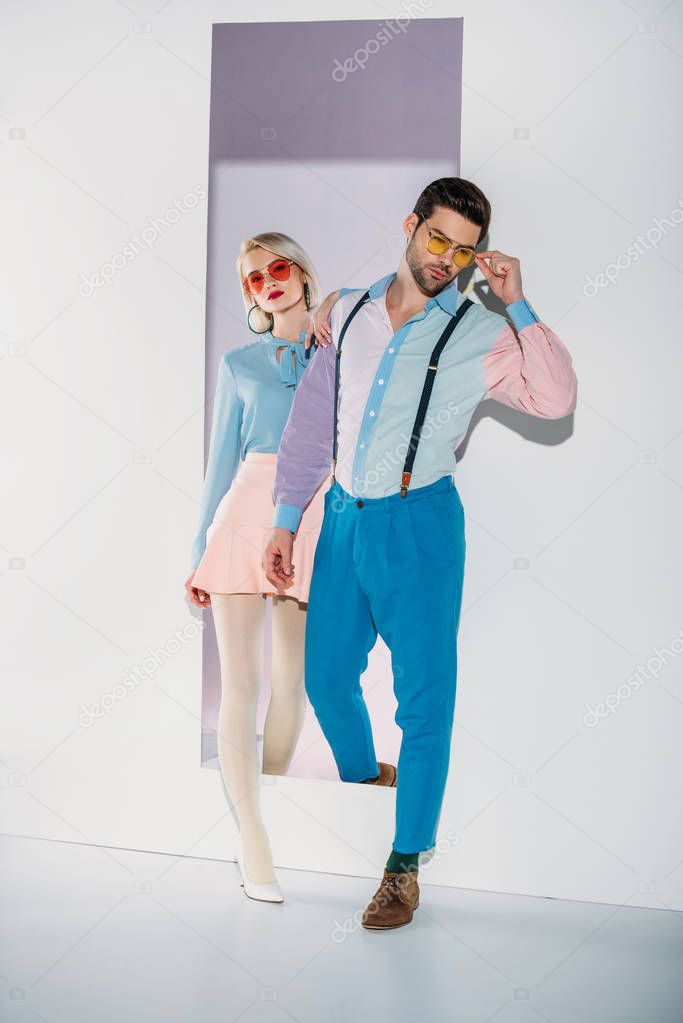 stylish young couple in sunglasses walking through aperture on grey 