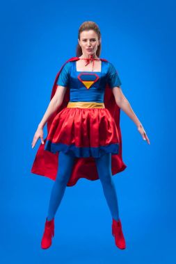 beautiful superwoman in costume jumping isolated on blue clipart