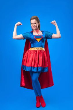 smiling woman in superhero costume showing muscles isolated on blue clipart