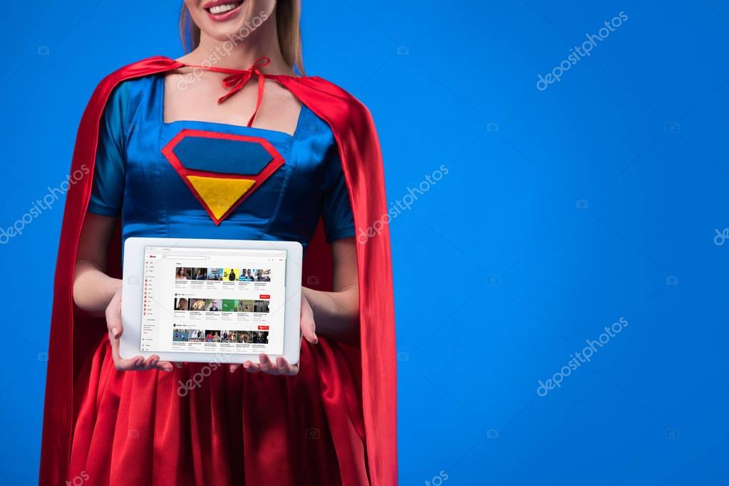 Cropped shot of woman in superhero costume showing tablet isolated on blue