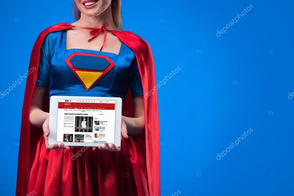 Cropped shot of woman in superhero costume showing tablet isolated on blue