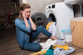 Hausfrau blickt zu Hause auf Kleiderstapel in Waschmaschine