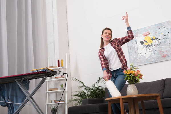 woman with dust cleaning brush listening to music while cleaning home