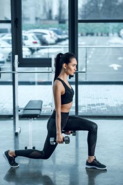 Genç uygun kadının tek bacak ağız kavgası vasıl jimnastik salonu dumbbells ile yapması yan görünüm