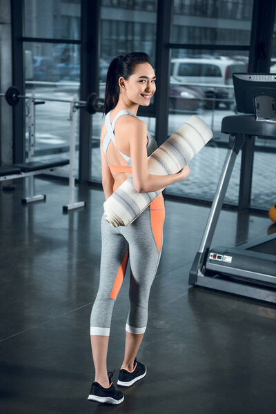 young fit woman with rolled yoga mat at gym