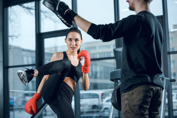 young female fighter performing low kick with trainer at gym