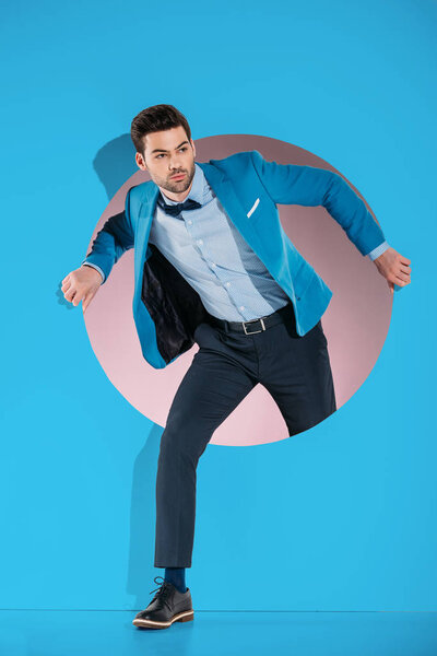 handsome man in fashionable clothes stepping through aperture on blue