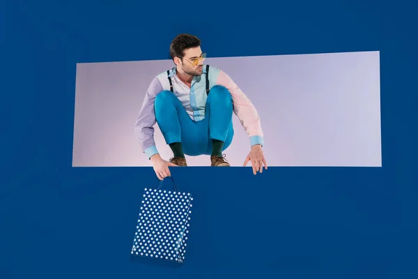 Handsome Man Stylish Clothes Squatting Shopping Bag Isolated Blue — Stock Photo, Image