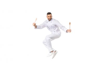 atlama ve üzerinde beyaz izole kamera gülümseyen mutfak eşyaları ile genç erkek Şef