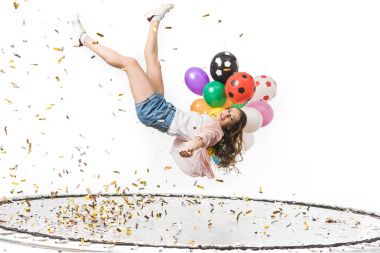 smiling girl holding colorful balloons and falling on trampoline isolated on white  clipart