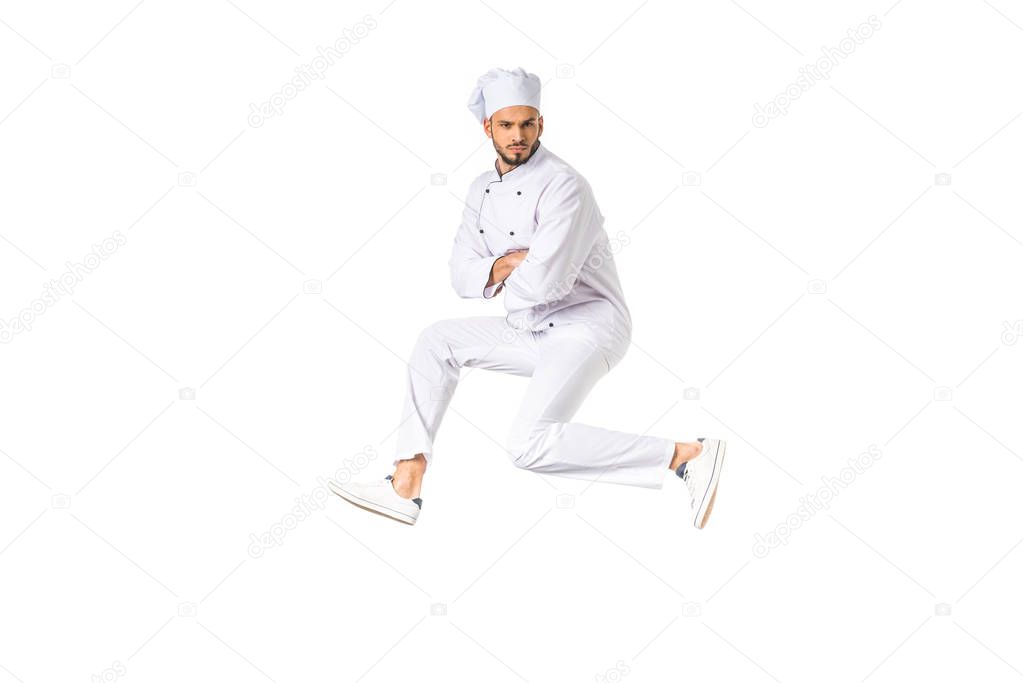 handsome young male chef jumping and looking at camera isolated on white